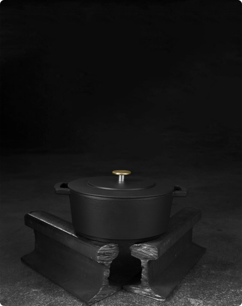 Zwarte gietijzeren pan met gouden knop gepresenteerd op twee industriële metalen balken tegen een donkere achtergrond.